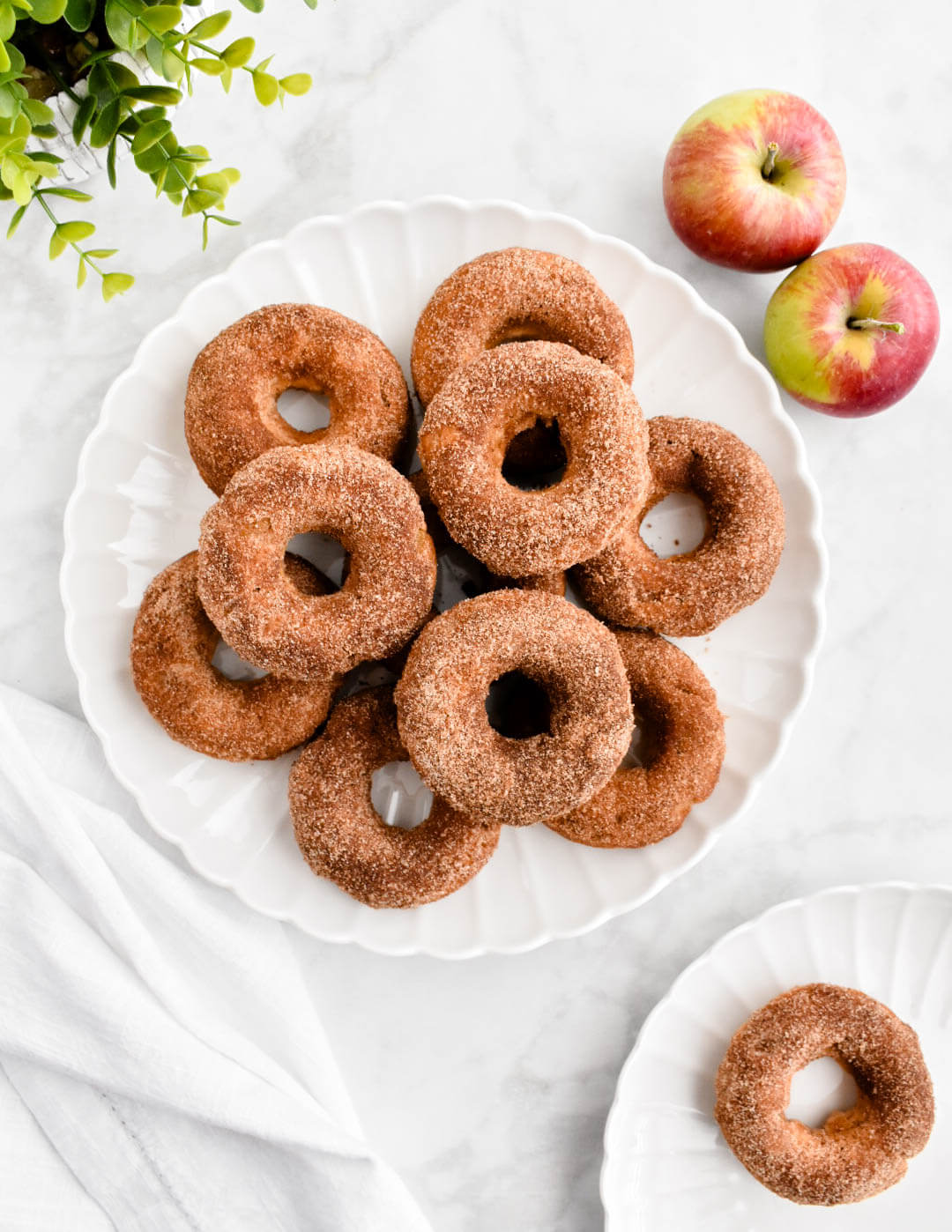 A platter of baked apple donuts set on a grey marble counter next to apples.