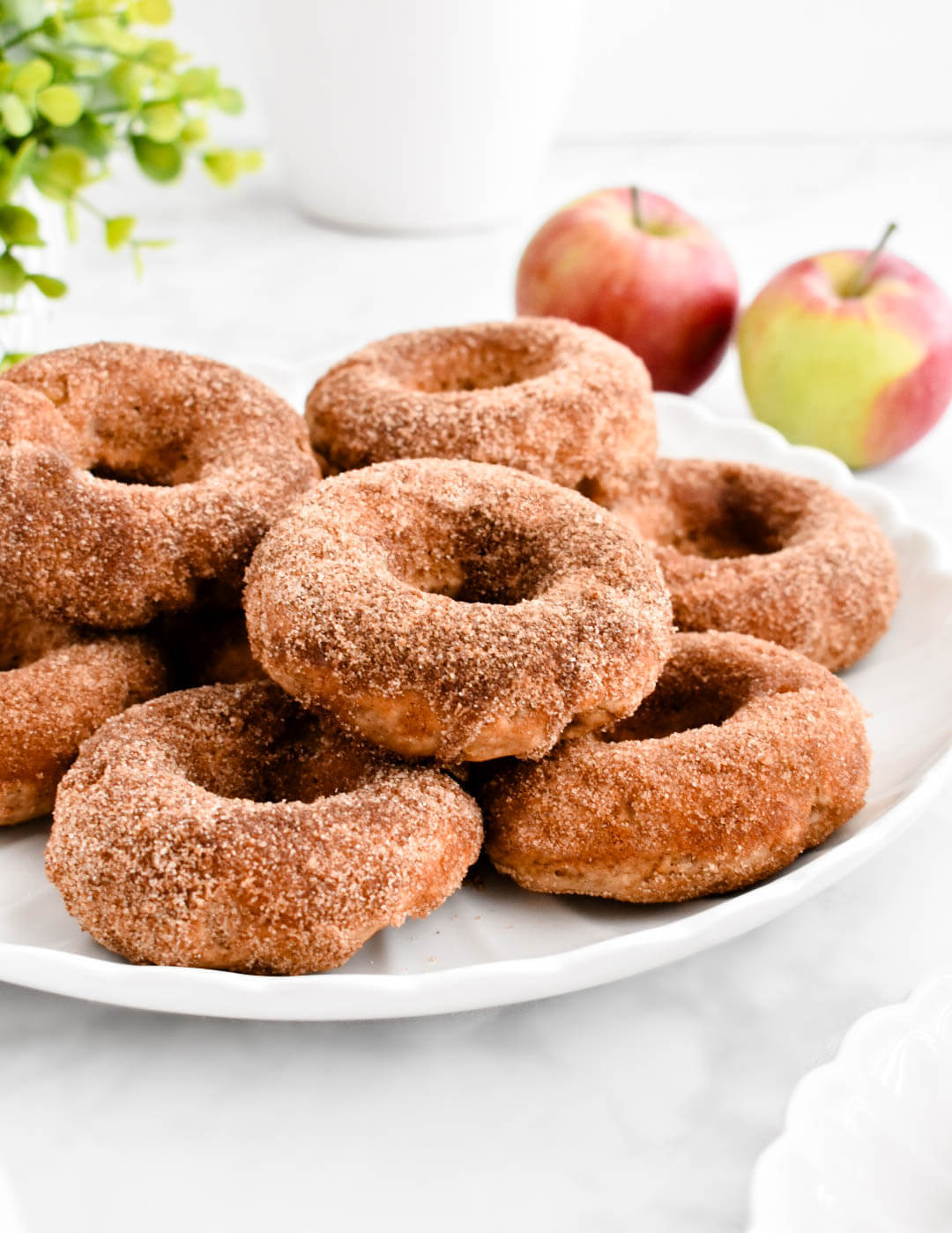 Baked apple donuts stacked on a white platter.