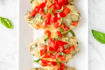 Platter with 4 Baked Pesto Chicken breasts topped with tomatoes and fresh basil.
