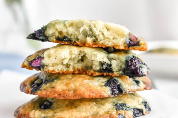 4 stacked blueberry muffin tops on parchment paper, the top muffin tops cracked in half.