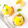 Plate of Caprese Eggs Benedict topped with fresh basil and served with lemon wedges.