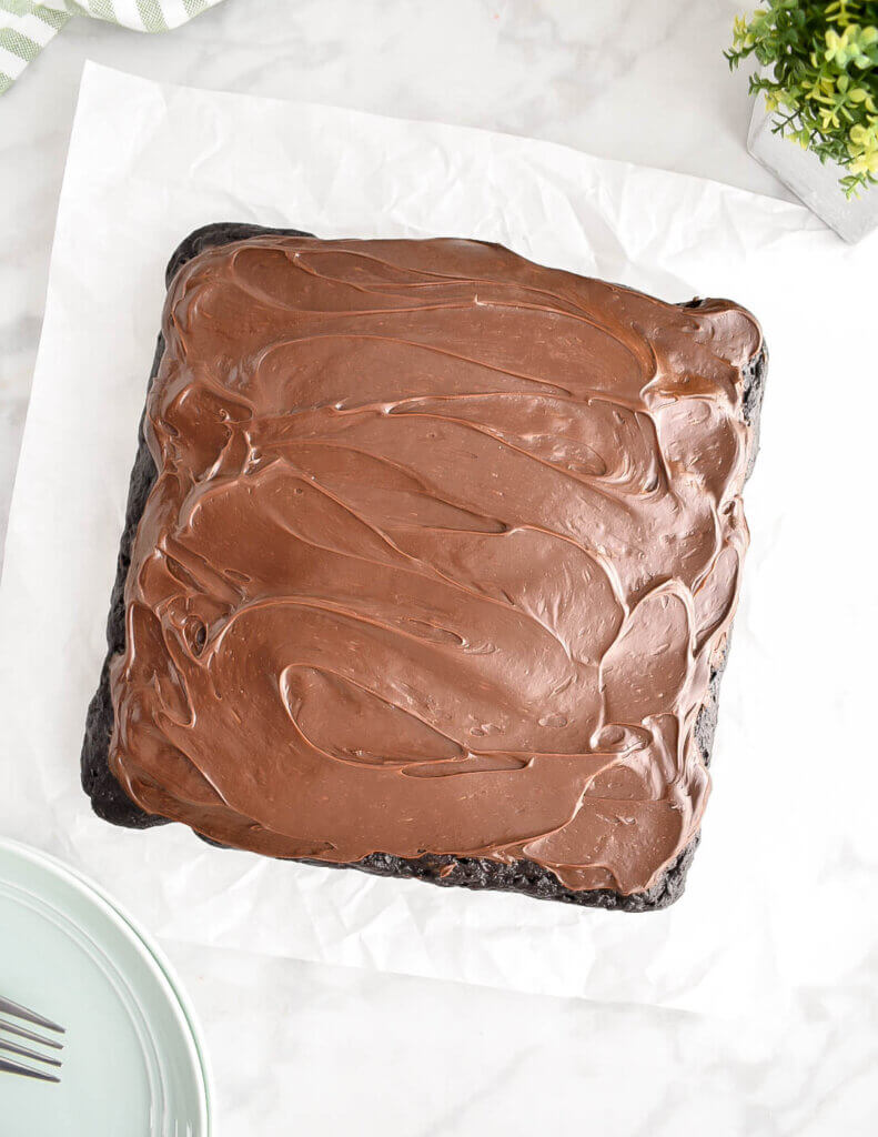 A chocolate frosted 9x9 inch chocolate zucchini cake on parchment paper.