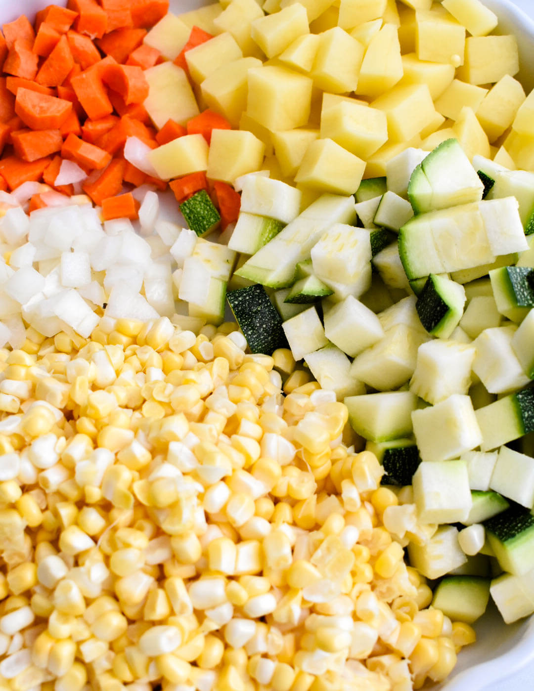 Chopped potato, carrot, zucchini, onion, and corn kernels prepared for the summer vegetable chowder.