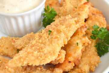 baked breaded homemade chicken fingers in a platter with fresh parsley and dip.