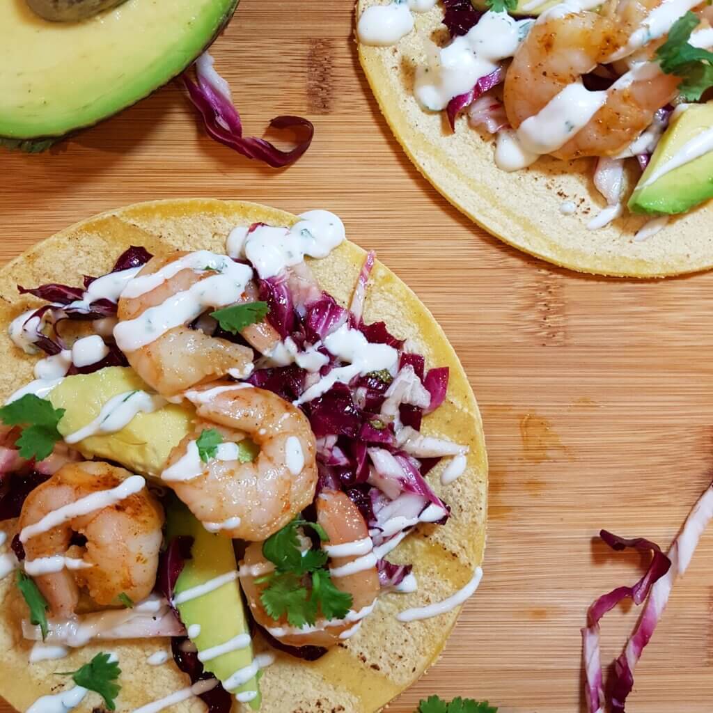Chili Lime Shrimp Tacos with Radicchio Slaw drizzled with cilantro sauce on a cutting board.
