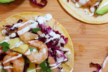 Chili Lime Shrimp Tacos with Radicchio Slaw drizzled with cilantro sauce on a cutting board.