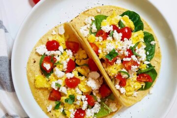A plate with two Mediterranean Breakfast Tacos filled with scrambled eggs, spinach, tomatoes and feta.