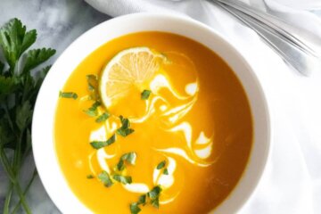 Bowl of Coconut carrot soup swirled with coconut milk and topped with fresh herbs and lime wedge.