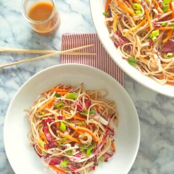 A large serving bowl filled with Soba Noodle Salad with Honey Sesame Dressing next to a small bowl of served up portion.