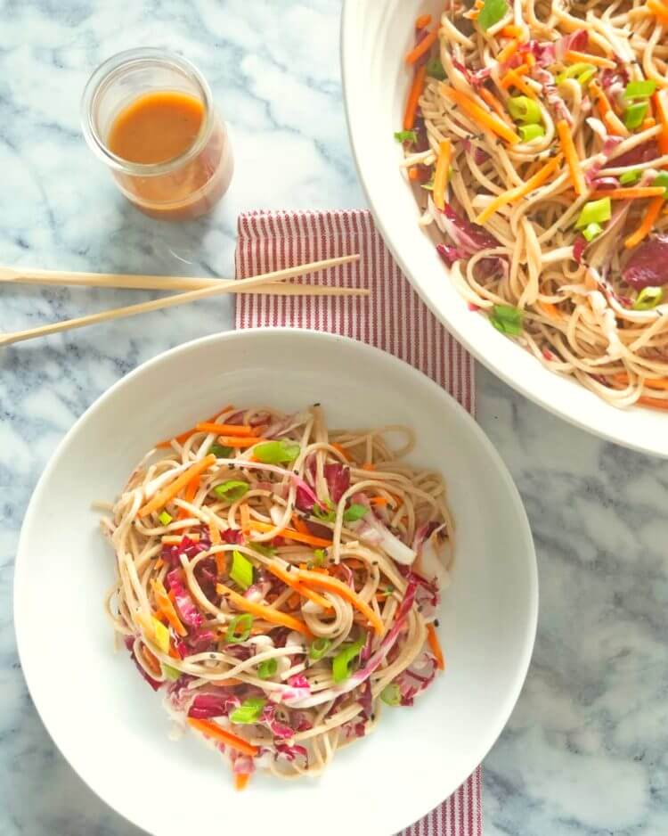 A large serving bowl filled with Soba Noodle Salad with Honey Sesame Dressing next to a small bowl of served up portion.