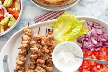 A chicken souvlaki platter with lettuce, red onion, and tomatoes served alongside pita.