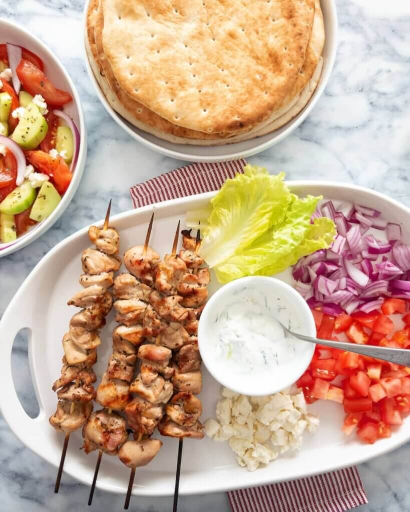 A chicken souvlaki platter with lettuce, red onion, and tomatoes served alongside pita.