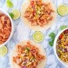 The Easiest Pulled Chicken Tacos on a kitchen counter with slices of lime.