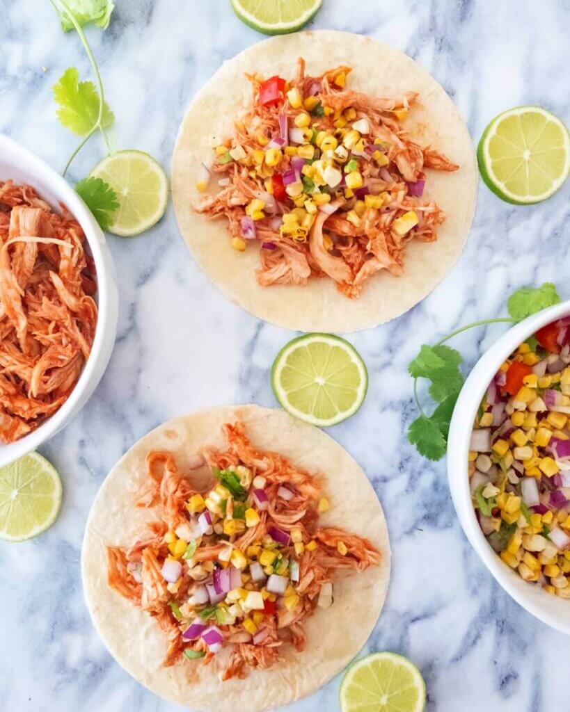 The Easiest Pulled Chicken Tacos on a kitchen counter with slices of lime.