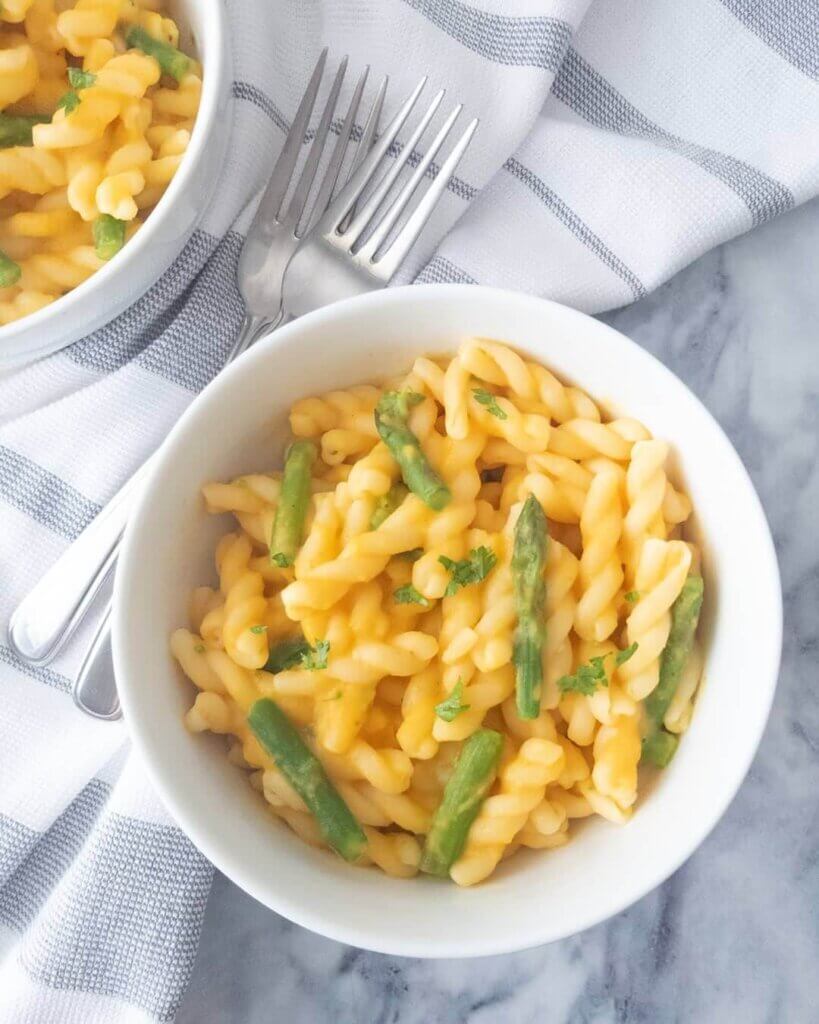 Bowls of Healthy Mac and Cheese with Asparagus set next to forks and napkins on a marble countertop.