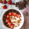 Bowl of yogurt topped with healthy dark chocolate granola and strawberries all drizzled with peanut butter.