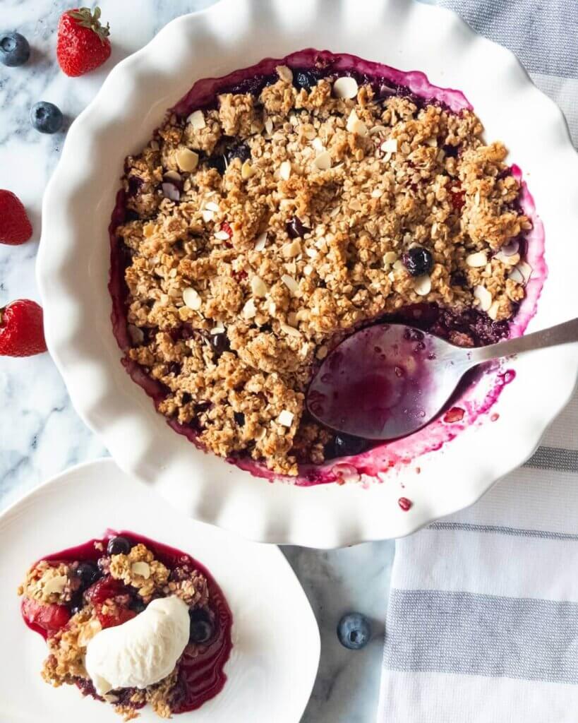 Healthy Berry Crisp in a baking dish next to a plated scoop of berry crisp.