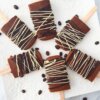 A square platter with Mocha Iced Coffee Popsicles drizzled with dark and white chocolate and surrounded by coffee beans.