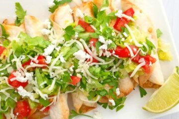 baked chicken taquitos topped with lettuce, shredded cheese and diced tomatoes