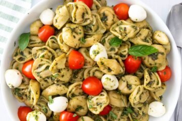 Caprese tortellini pasta salad in a bowl topped with fresh basil.
