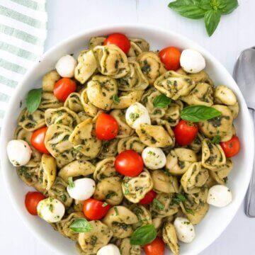Caprese tortellini pasta salad in a bowl topped with fresh basil.