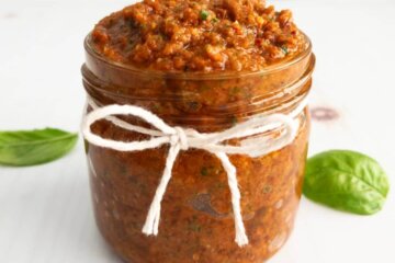 Sundried tomato pesto in a jar surrounded by fresh basil.