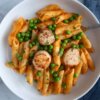 A plate of penne in a pumpkin sauce topped with peas and seared scallops.
