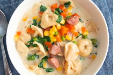 Creamy vegetable and tortellini soup in a bowl set on a blue napkin.