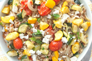 A bowl of Mediterranean Grain Salad with Roasted Summer Vegetables set on a yellow and white striped napkin.
