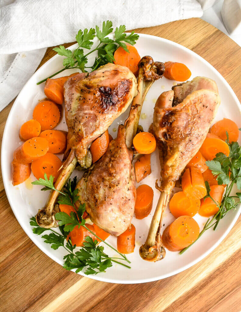 Roasted turkey drumsticks served on a white platter with carrot medallions and fresh parsley.