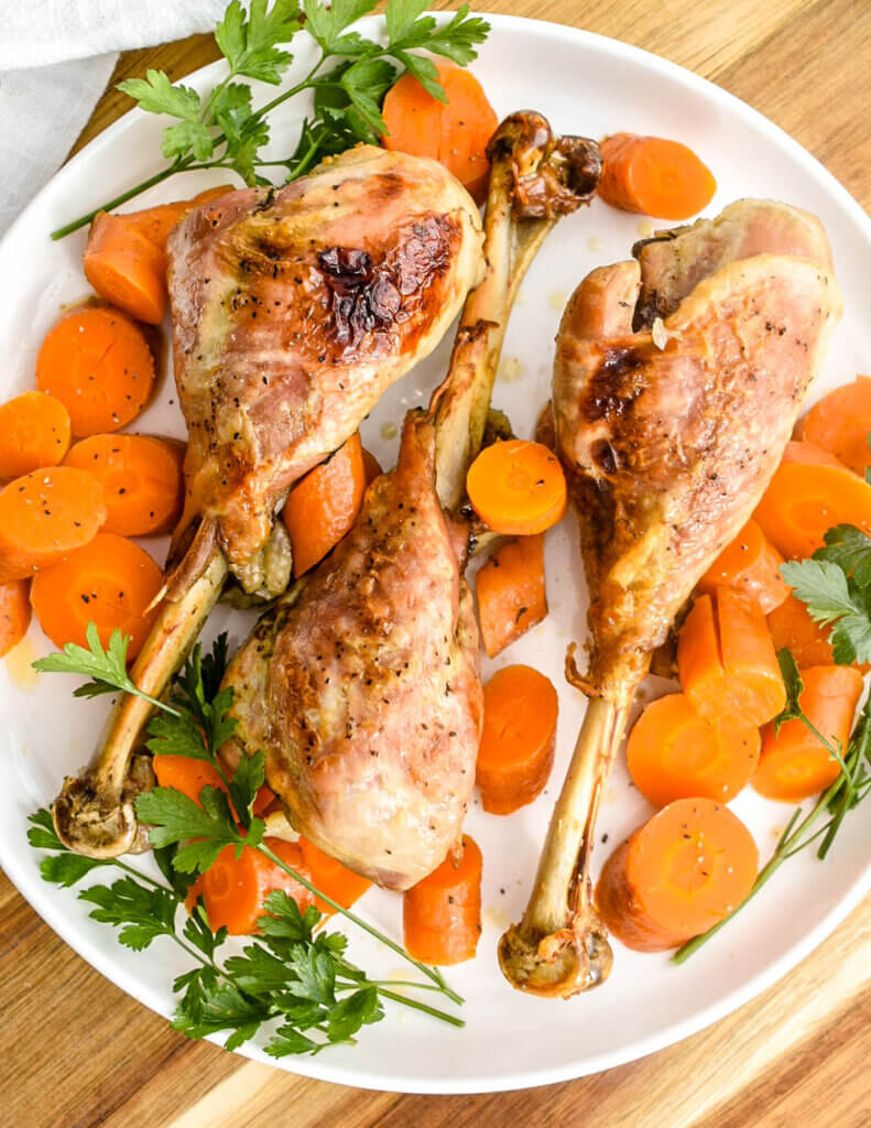 Closeup of roasted turkey drumsticks and carrot medallions and a white platter.