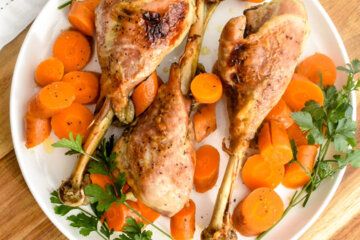A platter with three roasted turkey drumsticks and carrot medallions served with fresh parsley.
