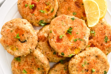 A platter of fresh salmon cakes sprinkled with parsley and served with lemon wedges.