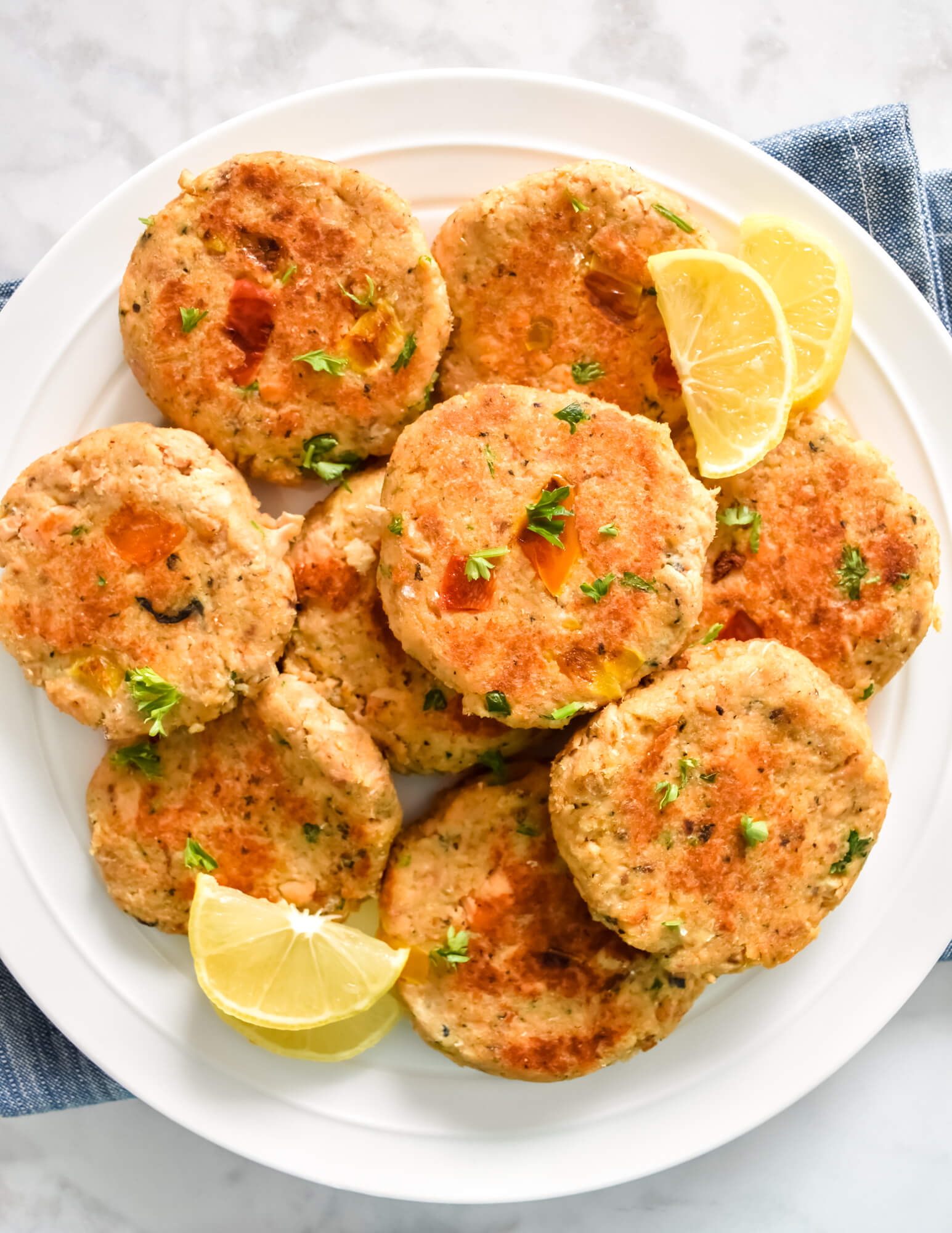 Closeup of a platter of fresh salmon cakes served with lemon wedges set on a blue cloth napkin.
