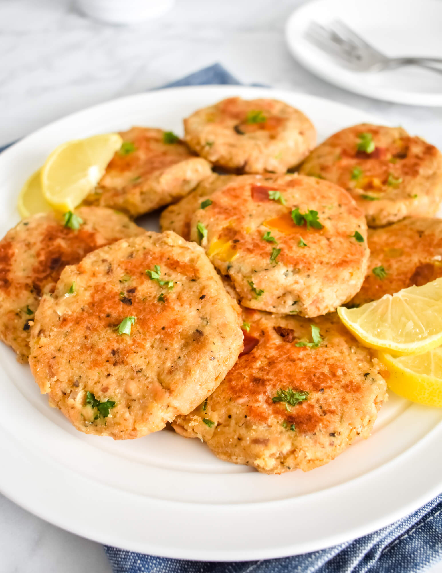Closeup of a pile of salmon patties served with lemon wedges on a white platter.