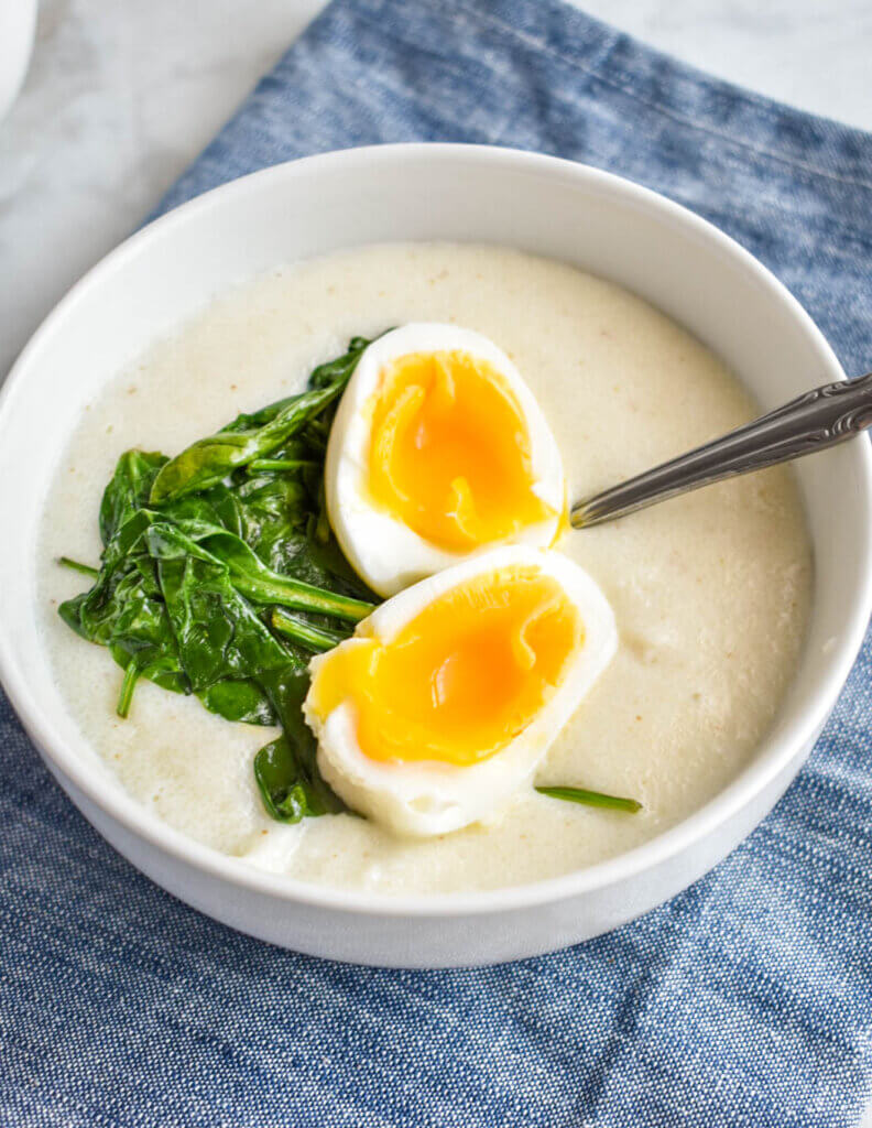 A bowl of semolina porridge with a jammy egg and sauteed spinach set on a blue napkin.