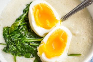 A bowl of savory semolina porridge topped with sauteed spinach and a jammy egg.