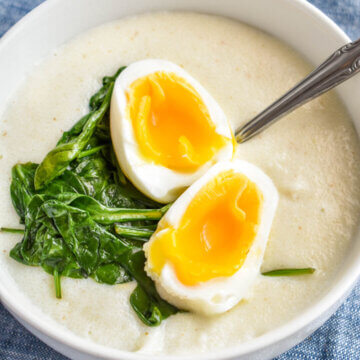 A bowl of savory semolina porridge topped with sauteed spinach and a jammy egg.