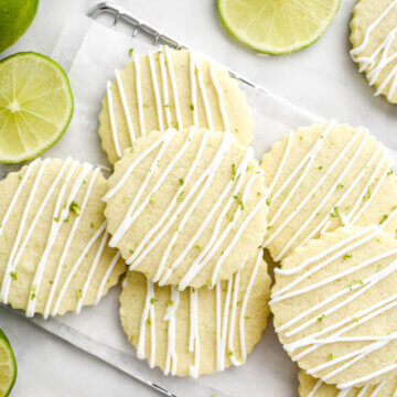 A pile of tequila and lime sugar cookies on a parchment lined cooling rack drizzled with royal icing and lime zest.