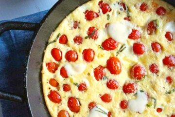 Cast iron skillet containing a Cherry Tomato Frittata studded with tomatoes and spotted with melted cheese.