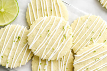 A pile of tequila and lime sugar cookies on a parchment lined cooling rack drizzled with royal icing and lime zest.