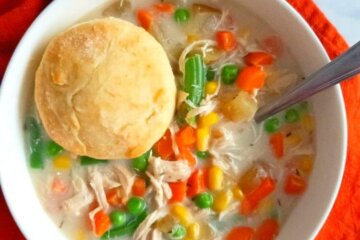 A bowl of Slow Cooker Chicken Pot Pie Soup topped with a biscuit set on an orange napkin.