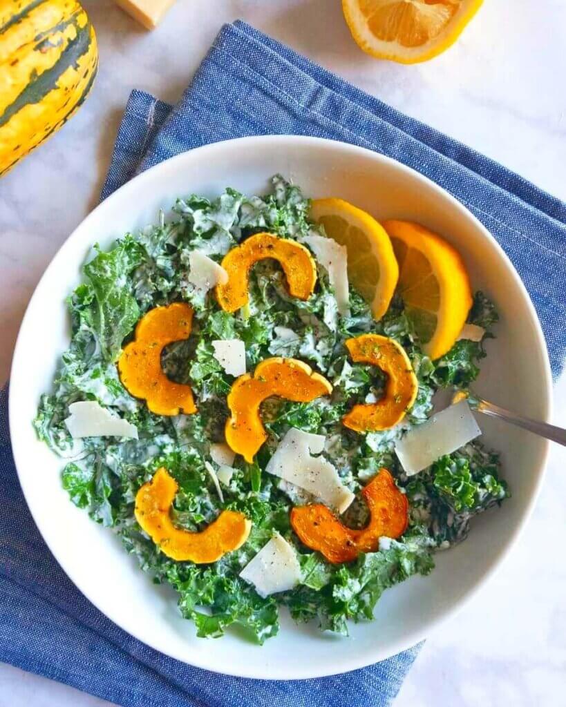 A bowl of Kale Caesar Salad with Roasted Delicata Squash on a blue napkin.