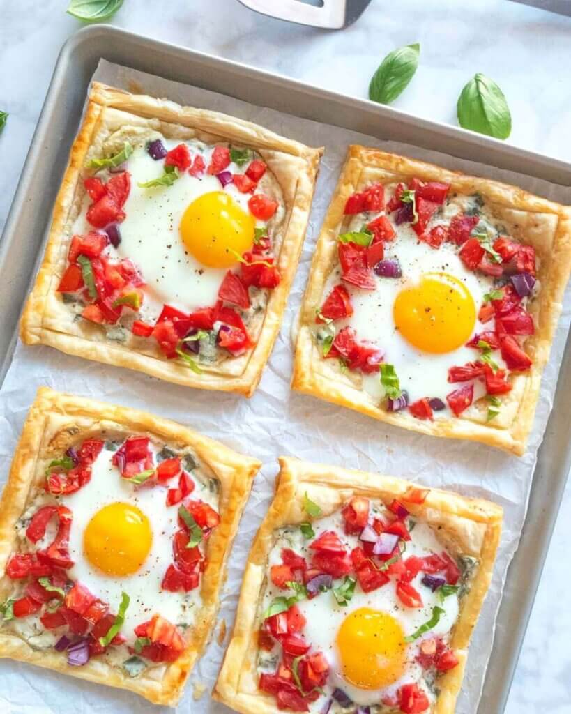 Baked tomato and egg breakfast tarts topped with chopped tomato and fresh herbs