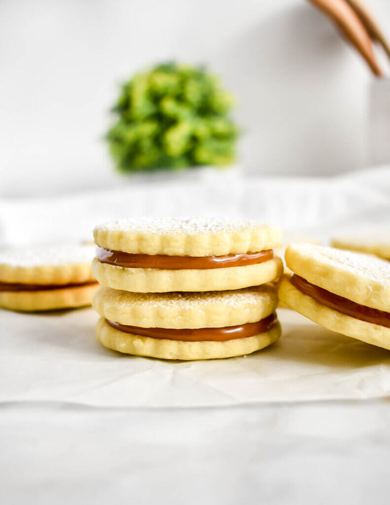 Two stacked dulce de leche sandwich cookies dusted with powdered sugar.