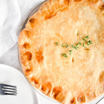 A chicken pot pie topped with sprigs of thyme on a marble countertop.