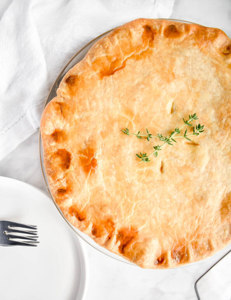A chicken pot pie topped with sprigs of thyme on a marble countertop.