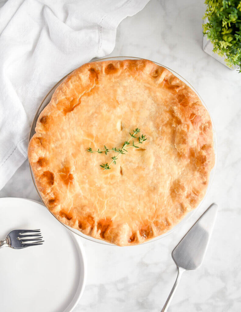 An unsliced chicken pot pie on a grey marble countertop set next to plates and a pie spatula.