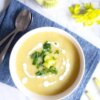 cream of celery soup in a bowl drizzled with yogurt and garnished with celery and herbs.