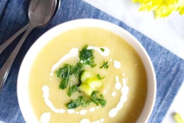 cream of celery soup in a bowl drizzled with yogurt and garnished with celery and herbs.